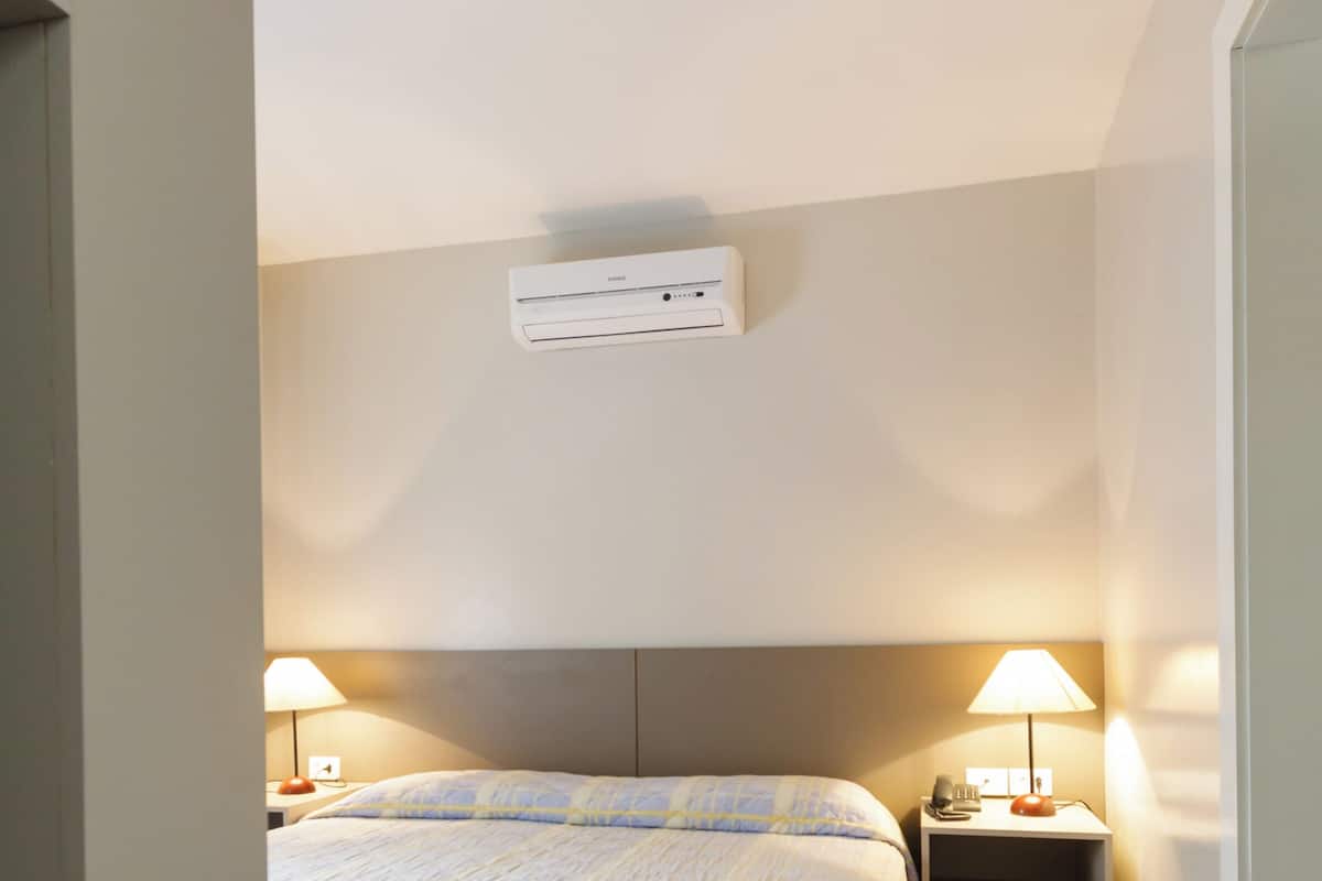 A bedroom with a bed, bedside lamps, a nightstand, and a ceiling vent.