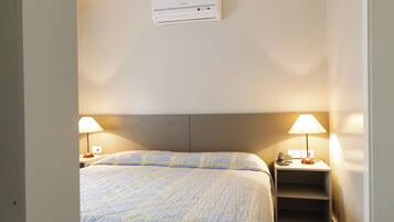 A bedroom with a bed, bedside lamps, a nightstand, and a ceiling vent.