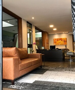 A modern hotel lobby with a leather sofa, a reception desk, and a large abstract painting on the wall.