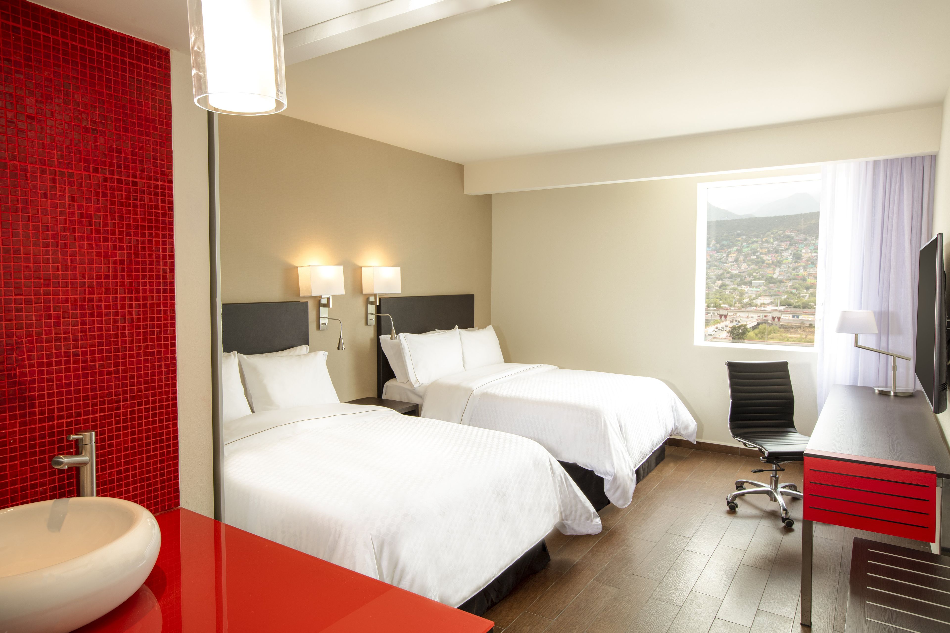 A hotel room with two beds, a desk with a chair, a television, and a window with a view.