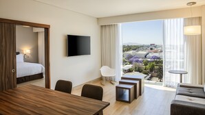 Ein Hotelzimmer mit Bett, Fernseher, Esstisch, Sofa und Blick auf die Stadt.