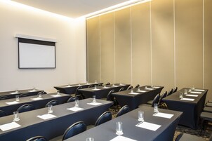 Un salón de conferencias con varias mesas, cada una con una pantalla de proyector, vasos y documentos.