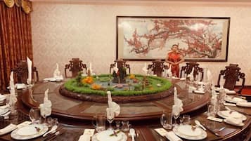 A round dining table with a central floral arrangement, surrounded by chairs and set with white tableware.