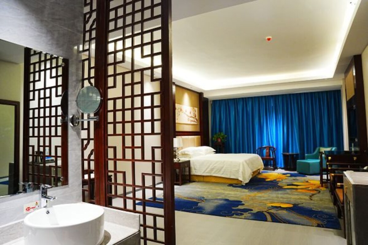 A hotel room with a large bed, a separate bathroom with a round mirror, and a decorative screen.