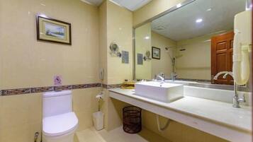 A bathroom with a toilet, sink, mirror, and a trash bin.