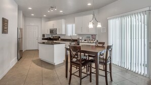 Una cocina moderna con armarios blancos, una isla central y una zona de comedor con sillas de madera.