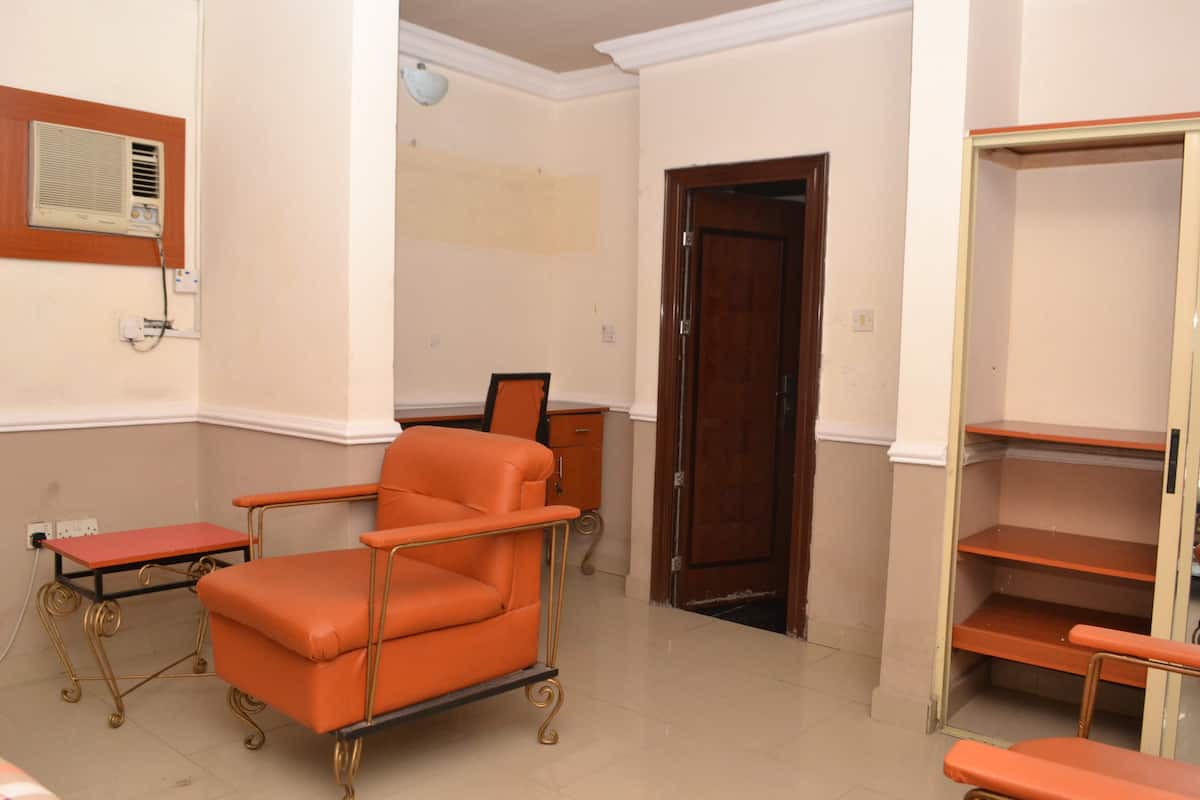 A room with a single orange chair, a wooden door, and a shelf unit.