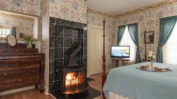 Una habitación con estufa de leña, cama con colcha azul, cómoda, televisor y papel tapiz floral.