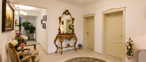 A hallway with ornate furniture, a mirror, and a chandelier.
