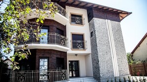 Un edificio moderno de dos pisos con fachada de piedra, balcones con barandas de hierro forjado y una vista despejada del entorno.