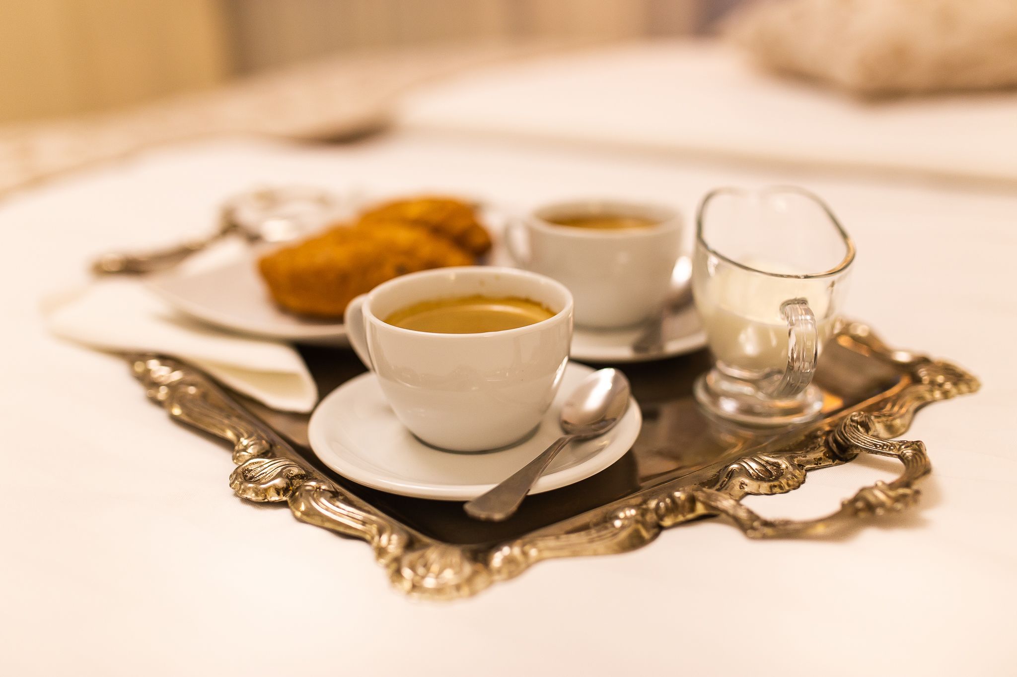 Una bandeja con una taza de café, un plato con pasteles y un vaso de agua sobre una mesa.