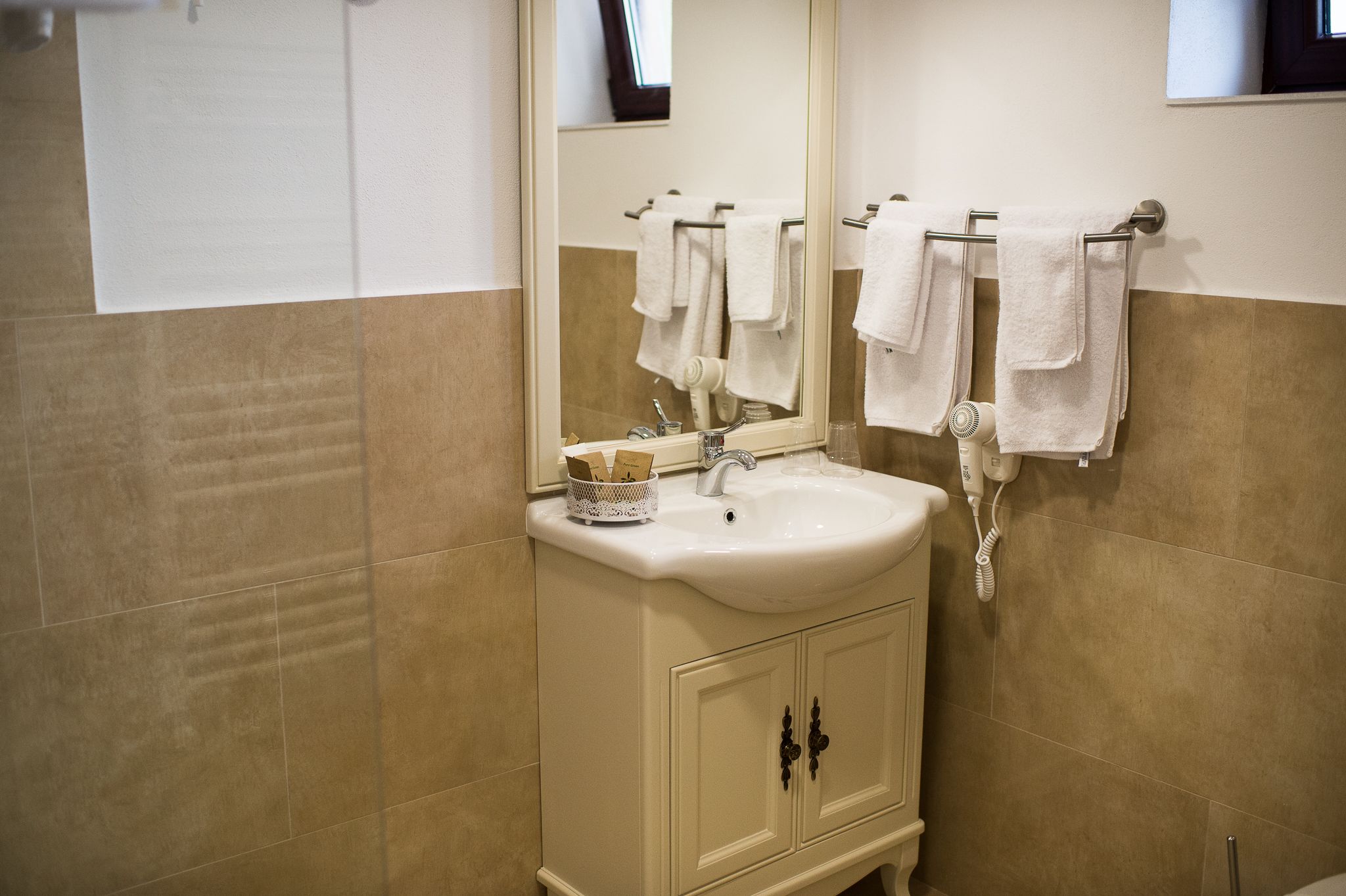A bathroom with a sink, mirror, towel rack, and a towel dispenser.