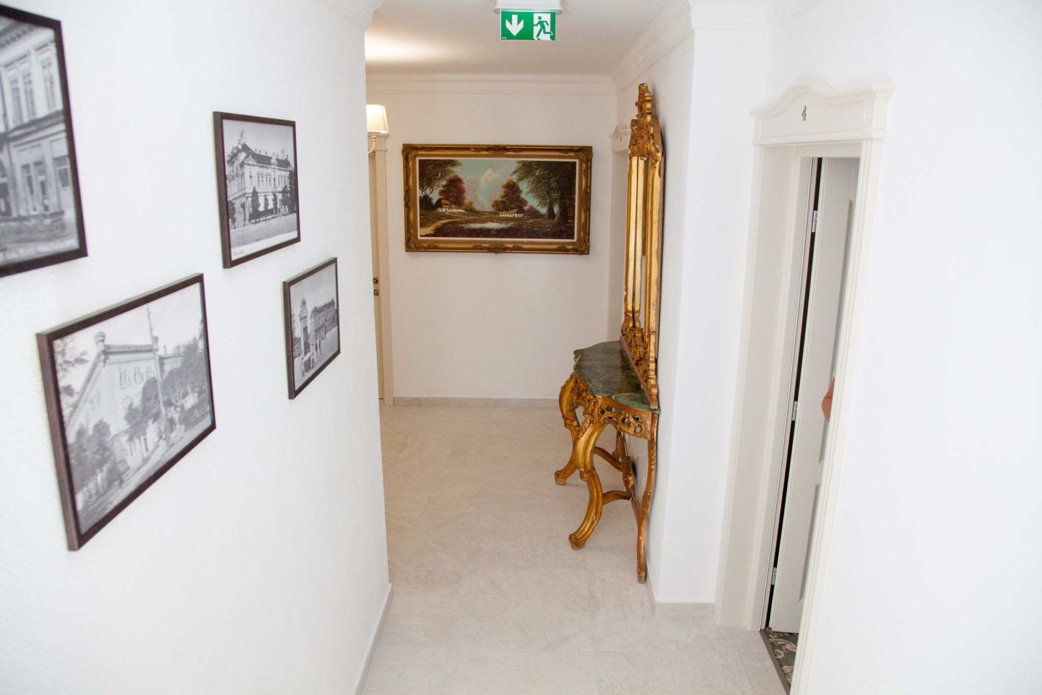 A hallway with framed pictures on the walls, a large landscape painting, and a golden chair.