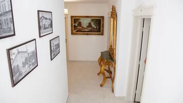 A hallway with framed pictures on the walls, a large landscape painting, and a golden chair.