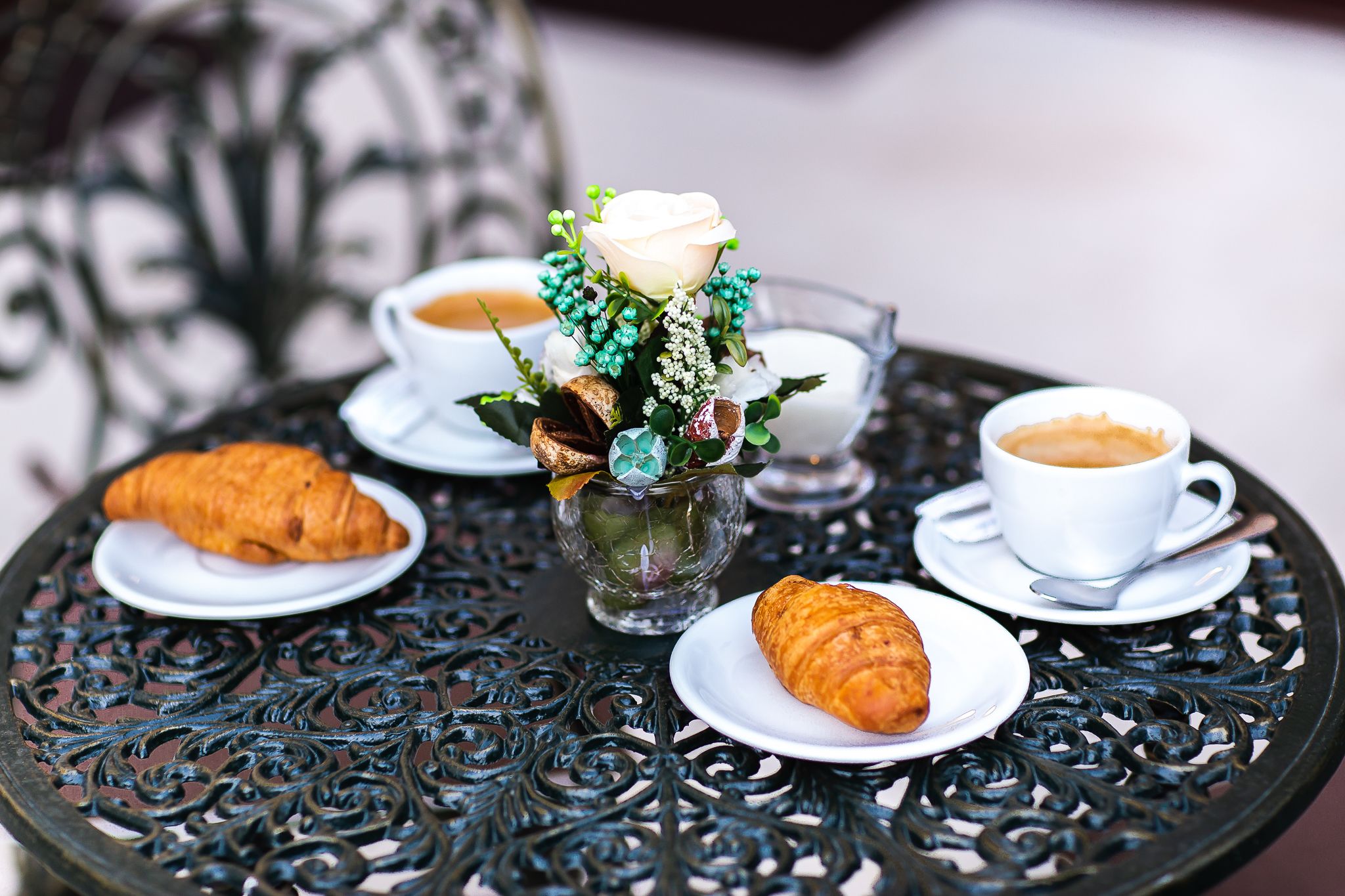 A table with a decorative centerpiece, two cups of coffee, and two croissants.
