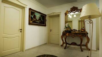 A hallway with cream-colored doors, a framed landscape painting, a mirror with an ornate frame, and a table with a floral arrangement.