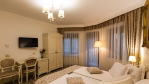 Habitación de hotel con dos camas, un escritorio, una silla, un televisor, un armario y una lámpara.