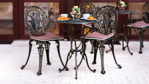 Un comedor con sillas y mesas de metal decorativo, un jarrón con flores y croissants sobre las mesas.