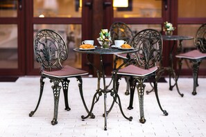 A dining area with ornate metal chairs and tables, a vase with flowers, and croissants on the tables. - Ave Alba (Alba Iulia)