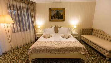 A hotel room with a large bed, two bedside tables, a bench, a painting on the wall, and a floor with a patterned carpet.