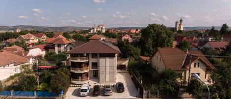 A residential area with a central building featuring a balcony and a parking area with cars.