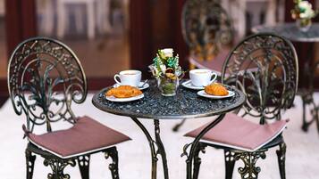 A round table with two chairs, each with a cup of coffee and a plate of croissants. A vase with flowers is on the table.