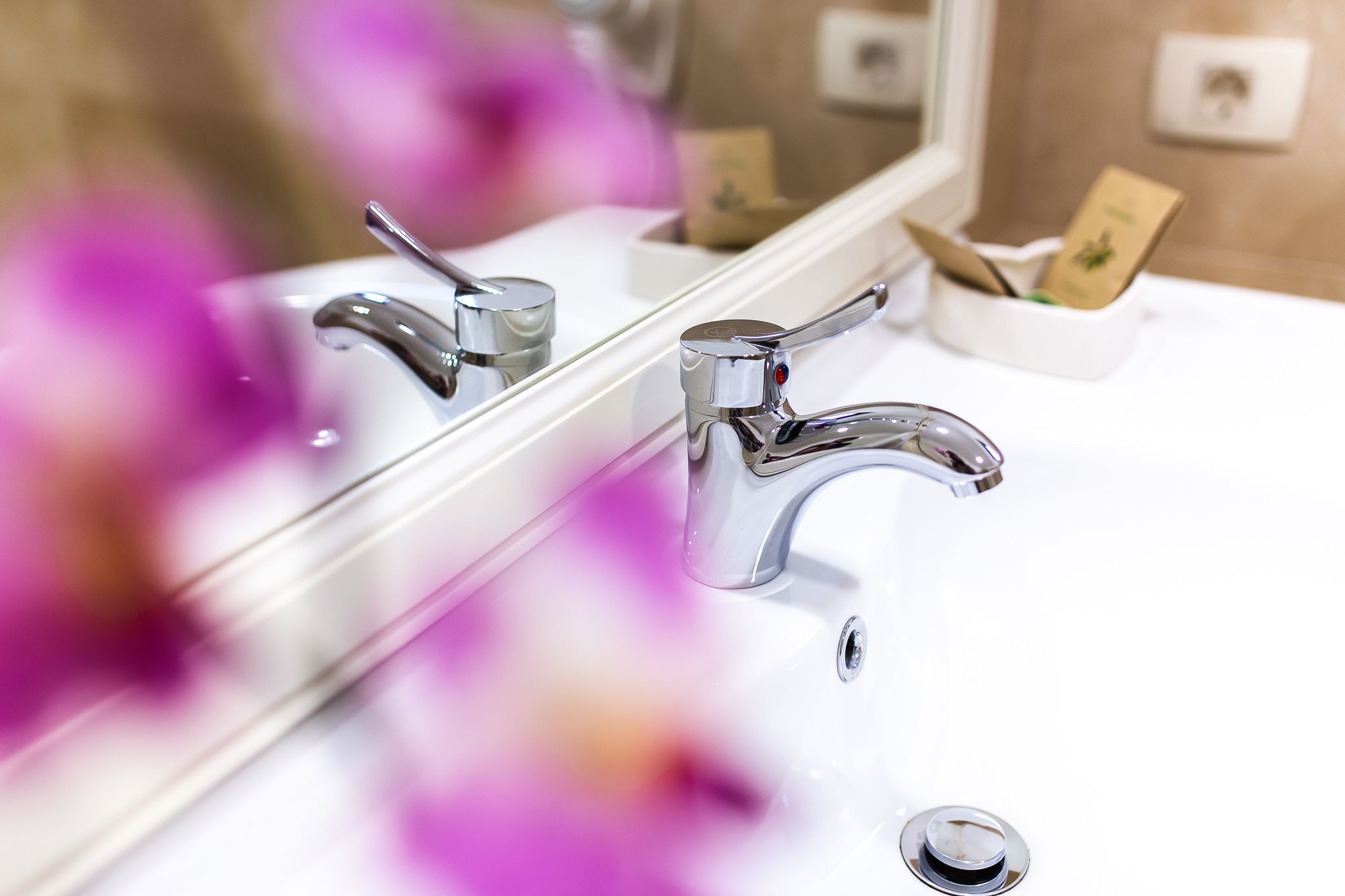 Un lavabo de salle de bain avec des robinets chromés et un miroir qui reflète une boîte de mouchoirs et une carte.