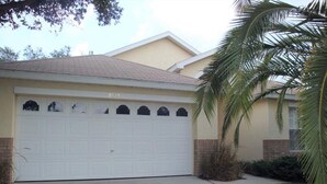 A two-story house with a large garage door, a sloped roof, and a small front yard with a palm tree.
