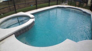 A swimming pool with a hot tub, surrounded by a fenced area and a grassy lawn.
