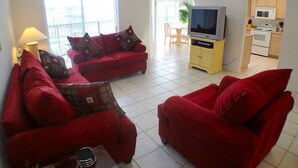 A living room with two red sofas, a television, and a kitchen area in the background.