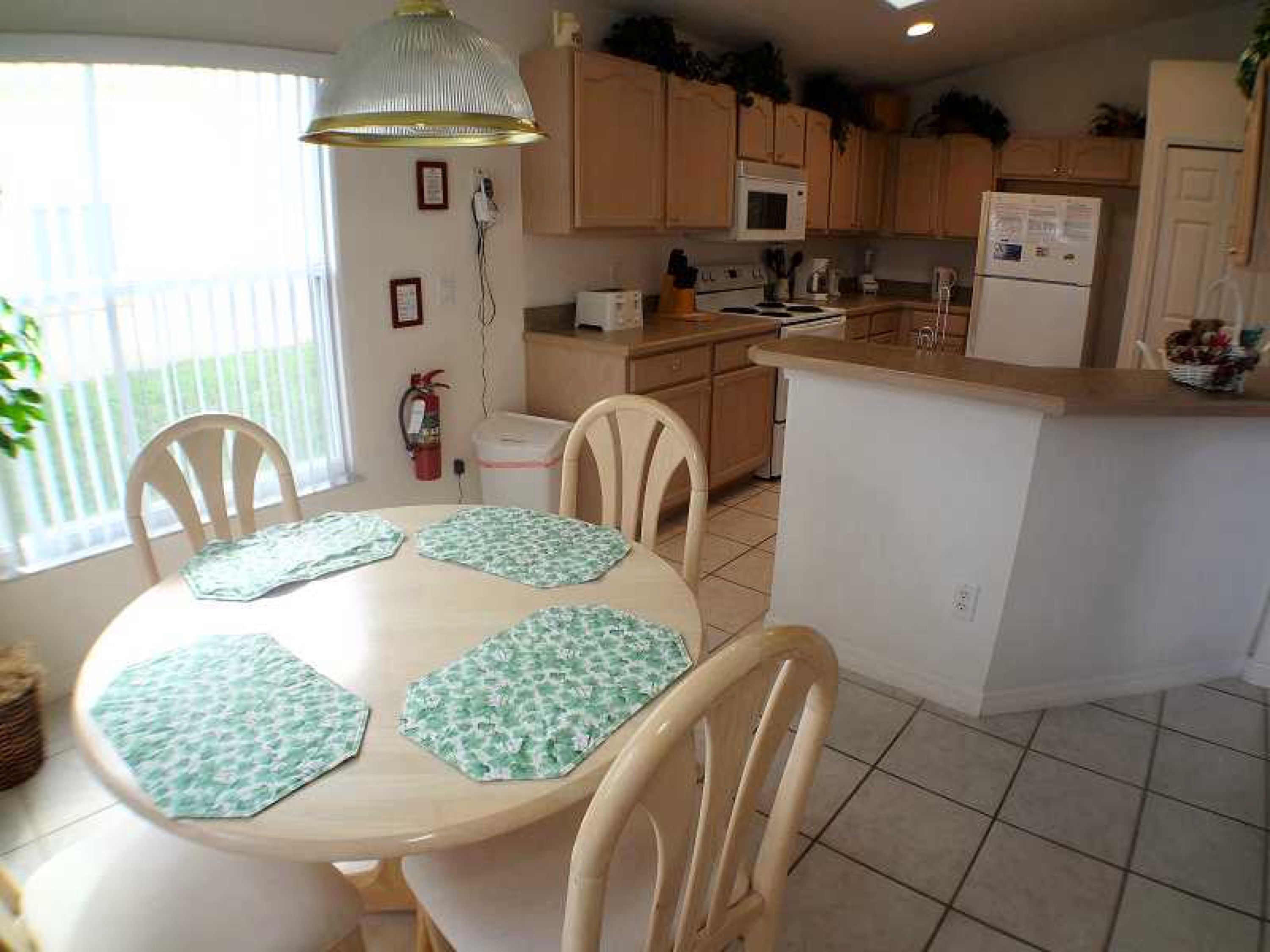 A kitchen with wooden cabinets, a microwave, a refrigerator, and a dining area with a table and chairs.