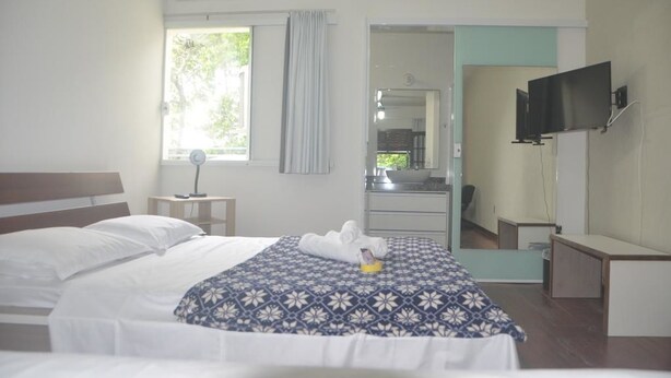 A hotel room with a bed, a desk, a TV, and a bathroom visible through an open door. - Hospedagem Praia de Piratininga (Niteroi)