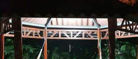 Un espacio de estar al aire libre con techo, una pérgola de madera, una hamaca y una mesa con sillas.