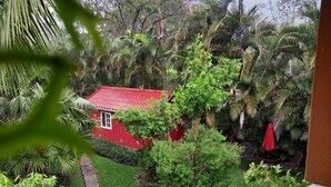 A red-roofed house surrounded by lush greenery, including various trees and shrubs.