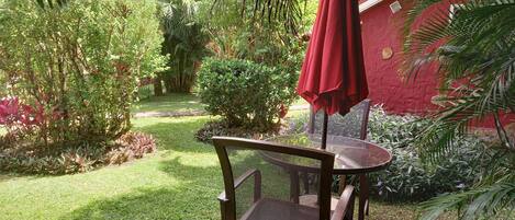 A garden with a table and chairs under a red umbrella.