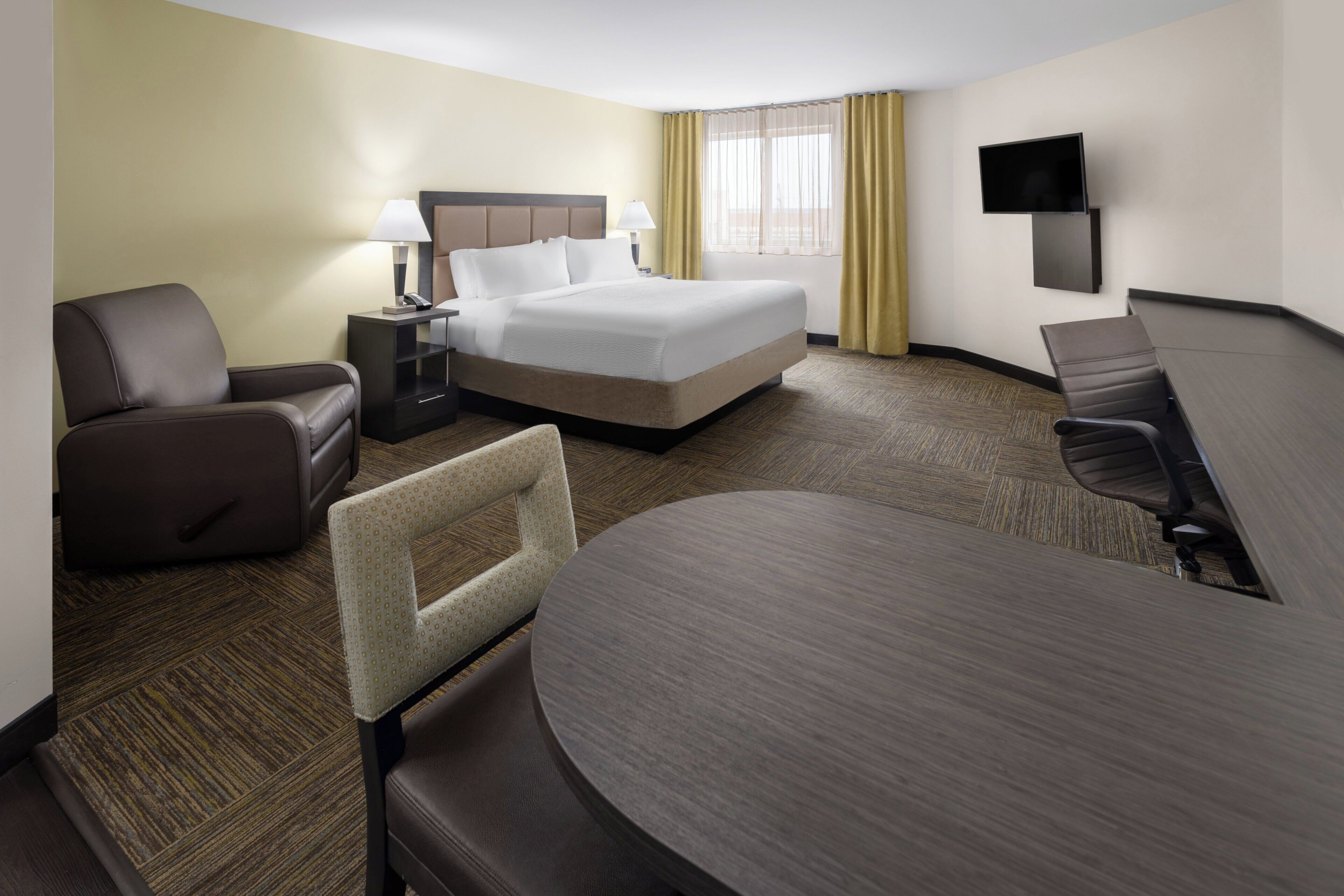 A hotel room with a bed, two armchairs, a desk, a television, and a window with curtains.