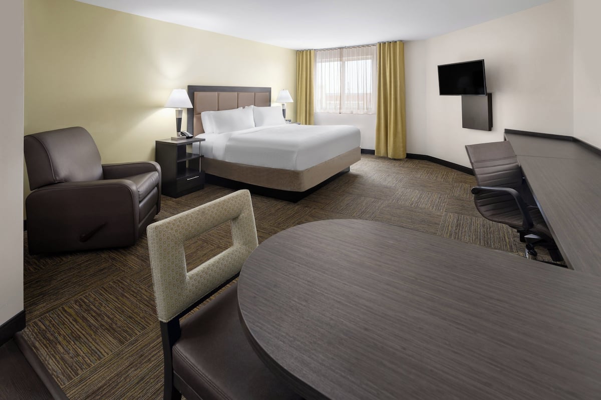Une chambre d’hôtel avec un lit, deux fauteuils, un bureau et une télévision.