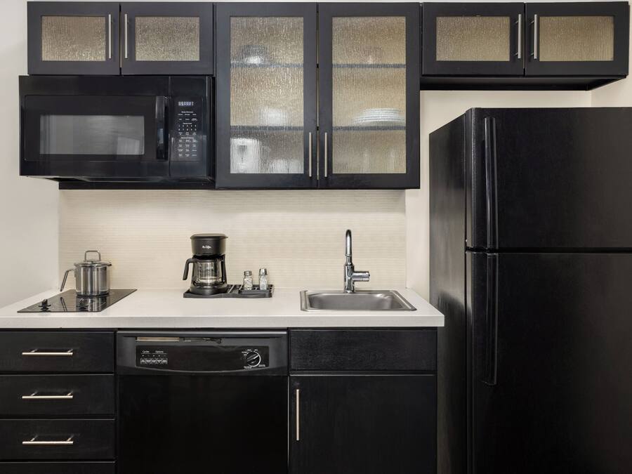 A kitchen with black cabinets, a microwave, a coffee maker, a sink, and a dishwasher.