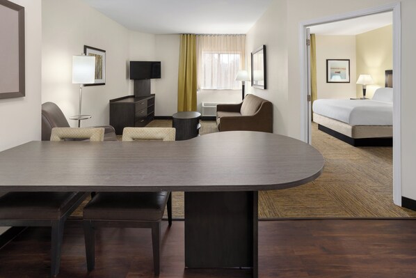 A hotel room with a large bed, a desk with a chair, a sofa, a TV, and a small table.