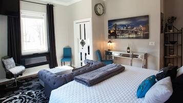 A hotel room with a bed, a desk, a chair, a sofa, a fireplace, and a cityscape painting on the wall.