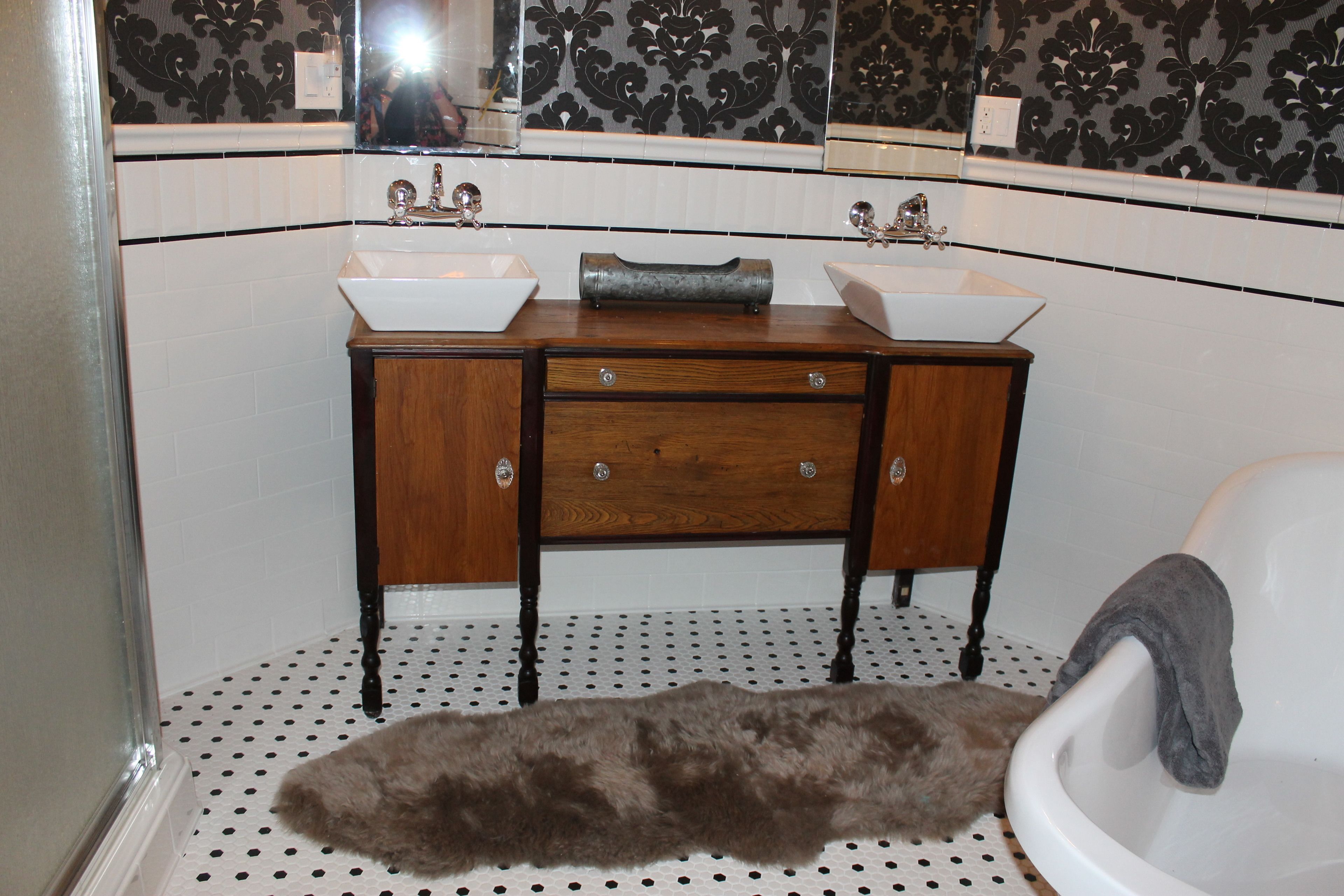 A bathroom with a wooden vanity, two sinks, a mirror, and a polka dot floor.