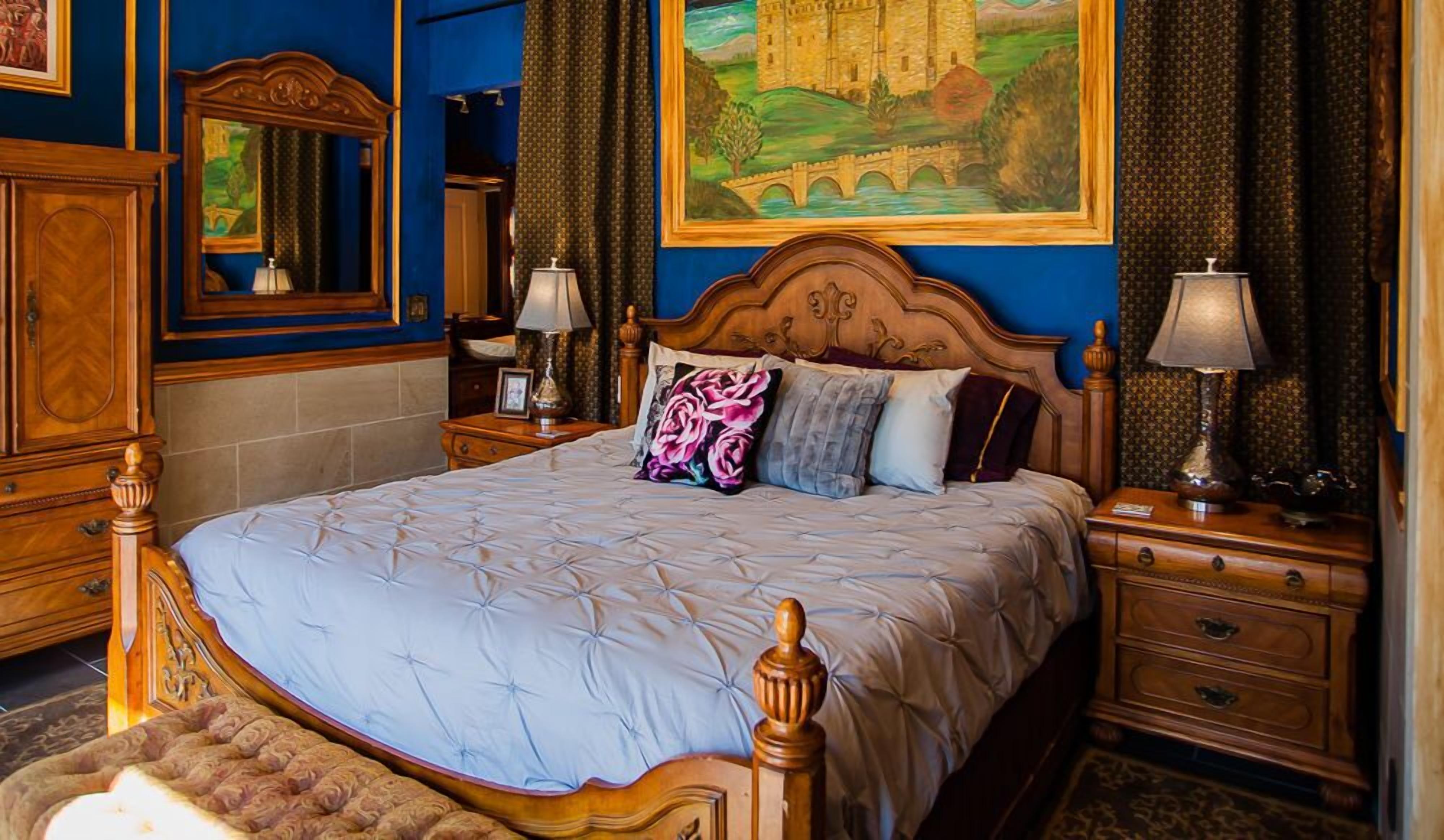 Un dormitorio con una cama grande, cabecera de madera, dos mesitas de noche con lámparas, un espejo y un cuadro en la pared.