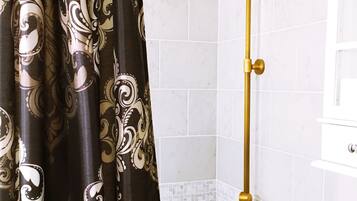 Een badkamer met een douche, witte betegelde muren en een decoratief gordijn.