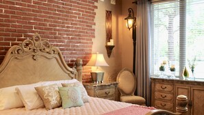 Ein Schlafzimmer mit Backsteinwand, einem hölzernen Bett mit verziertem Kopfteil, einem Nachttisch mit Lampe, einer Kommode mit Schubladen und einem Fenster mit Vorhängen.