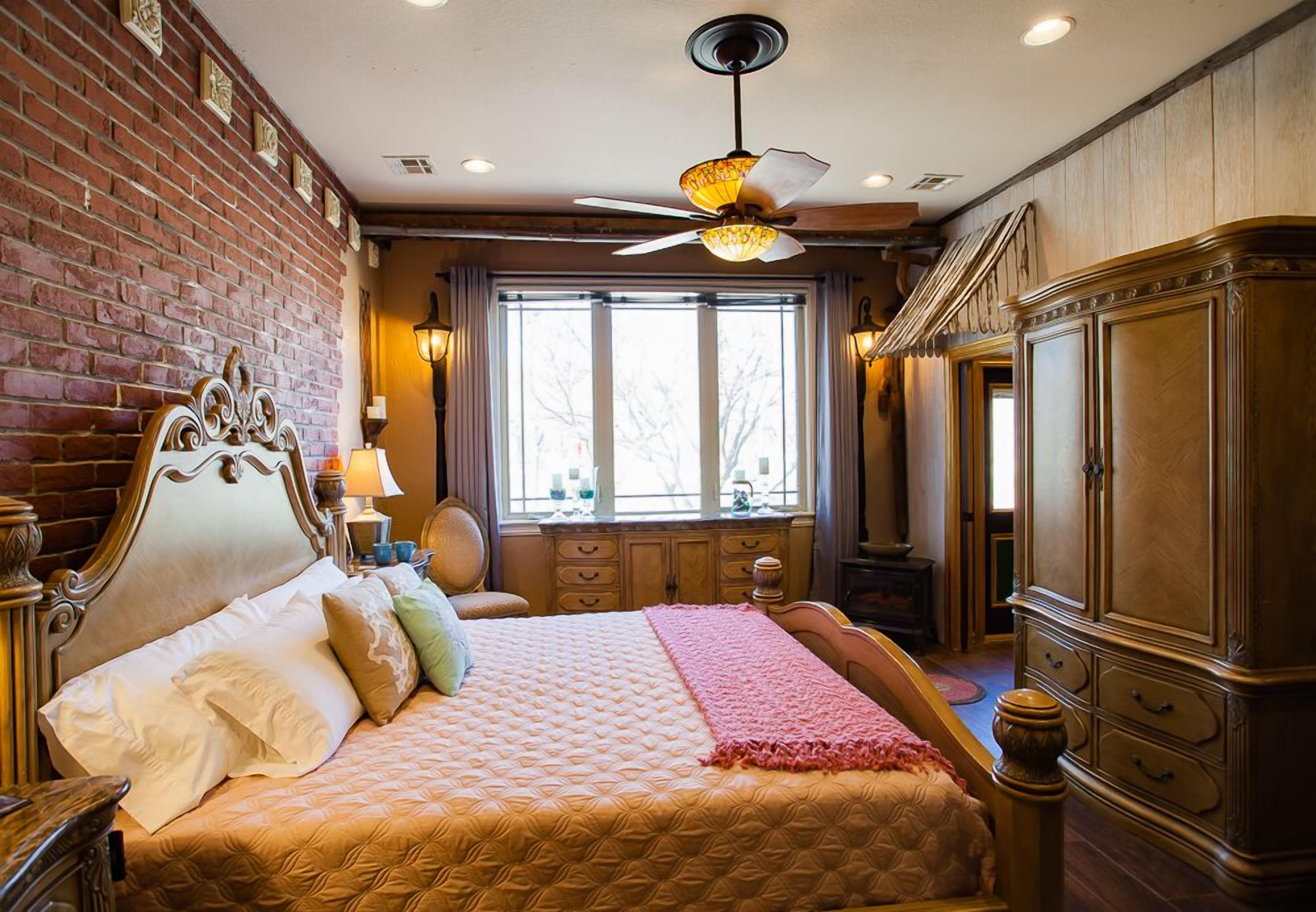 Une chambre avec un grand lit, une armoire en bois, un mur en briques et une fenêtre donnant sur un beau paysage.