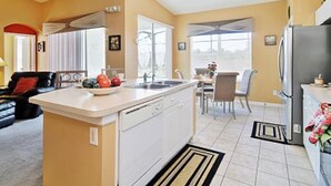 Uma cozinha compacta com uma ilha central, uma área de refeições com mesa e cadeiras, e uma geladeira.