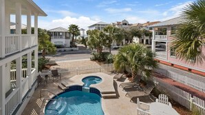 A swimming pool with a hot tub, surrounded by a white fence, palm trees, and a view of other buildings. - The Love Shack (Panama City Beach)