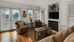 A living room with a fireplace, wicker furniture, and a television. - The Love Shack (Panama City Beach)