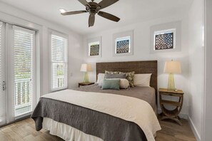 A bedroom with a large bed, two bedside tables with lamps, a ceiling fan, and a view through the window blinds.