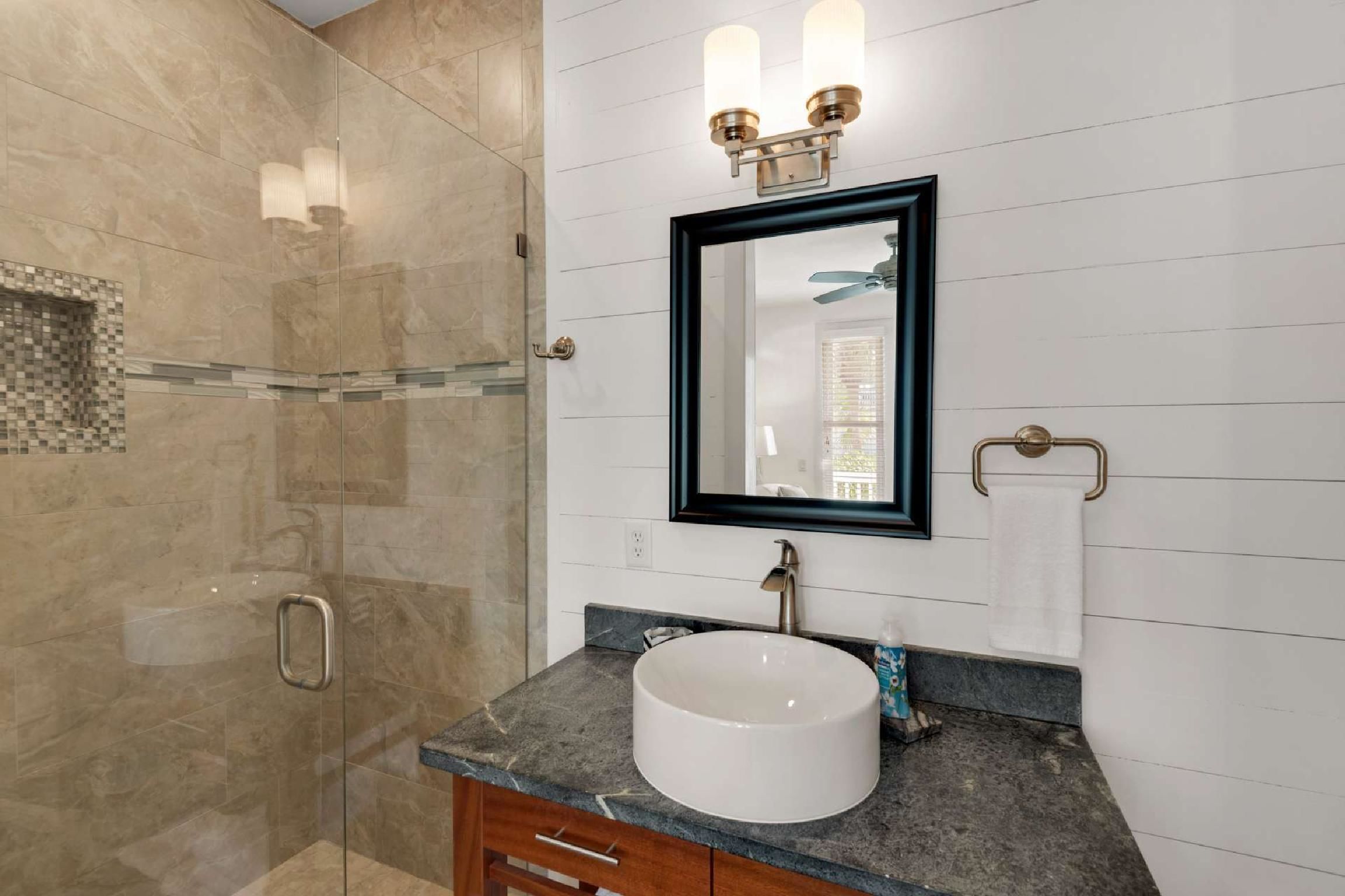 A modern bathroom with a glass shower enclosure, a white sink, and a vanity with a marble countertop.